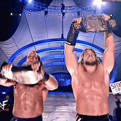 Two Wrestlers Holding Up Championship Belts GIF