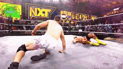 Two Wrestlers In A Ring With A Sign That Says Nxt Behind Them GIF
