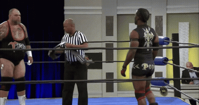 Two Wrestlers In Ring With Referee Holding Remote GIF