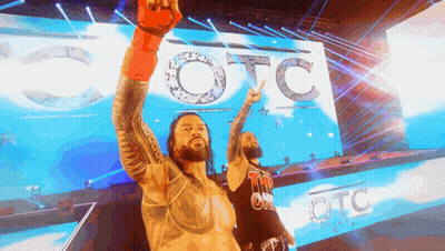 Two Wrestlers Standing In Front Of A Large Screen That Says Otc GIF