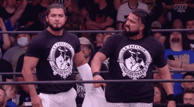 Two Wrestlers Wearing Black Shirts That Say La Facción GIF