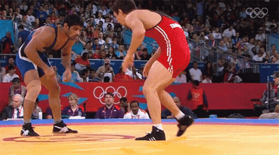 Two Wrestlers Wrestling In Front Of Crowd With Olympic Rings GIF