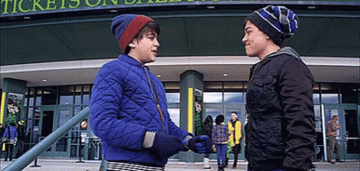 Two Young Boys Are Shaking Hands In Front Of A Building That Says Tickets On It GIF