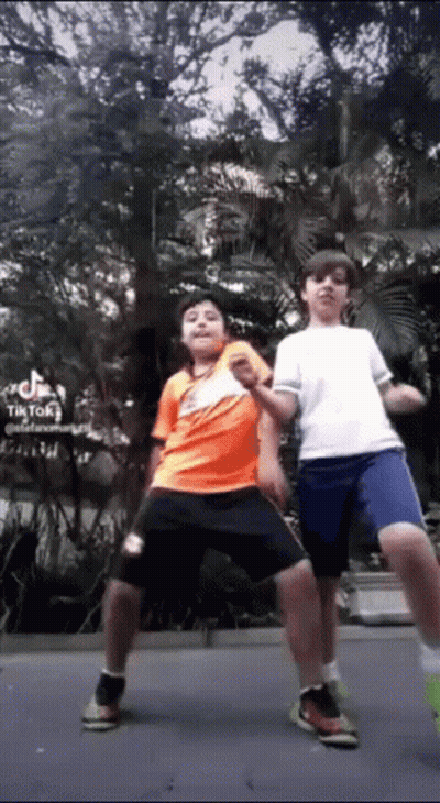 Two Young Boys Are Standing Next To Each Other In A Park And Dancing . GIF