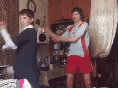 Two Young Men Are Dancing In A Living Room With A Clock In The Background . GIF