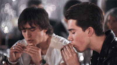 Two Young Men Are Eating Hamburgers In A Restaurant . GIF
