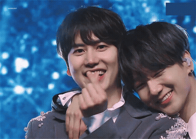Two Young Men Are Hugging Each Other And One Of Them Is Making A Heart Shape With His Finger GIF