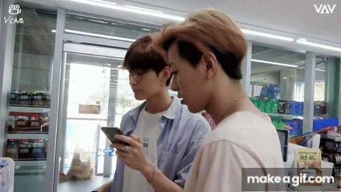 Two Young Men Are Looking At Their Cell Phones In A Store With The Words Make A Gif.com On The Bottom Right GIF