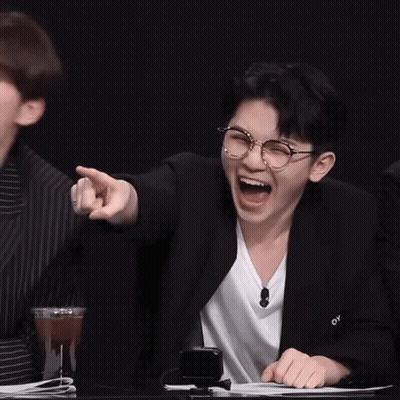 Two Young Men Are Sitting At A Table Laughing And Pointing At Something . GIF