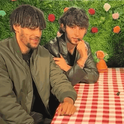 Two Young Men Are Sitting At A Table With A Checkered Tablecloth . GIF
