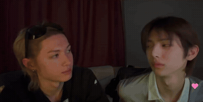 Two Young Men Are Sitting Next To Each Other And Looking At Each Other In A Dark Room . GIF