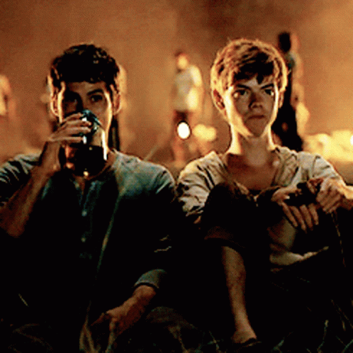 Two Young Men Are Sitting Next To Each Other Drinking From Glasses GIF