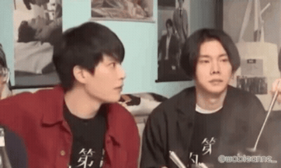 Two Young Men Are Sitting Next To Each Other In A Living Room . GIF