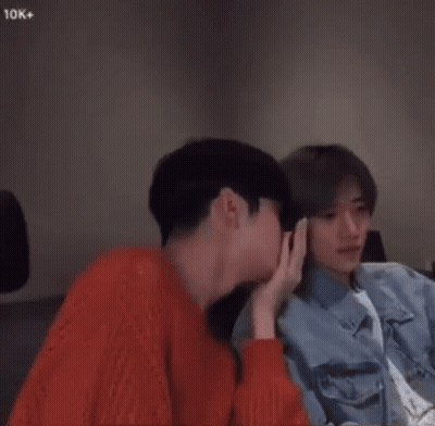 Two Young Men Are Sitting Next To Each Other In A Room And Holding Hands . GIF