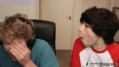 Two Young Men Are Sitting Next To Each Other In A Room . One Of The Men Is Covering His Face With His Hand . GIF