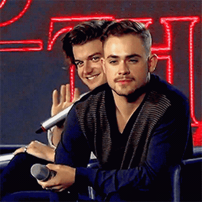 Two Young Men Are Sitting Next To Each Other In Front Of A Microphone . GIF