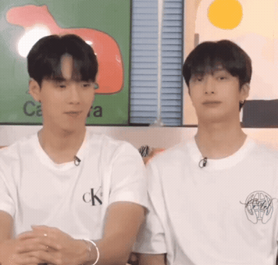 Two Young Men Are Sitting Next To Each Other In Front Of A Wall . GIF