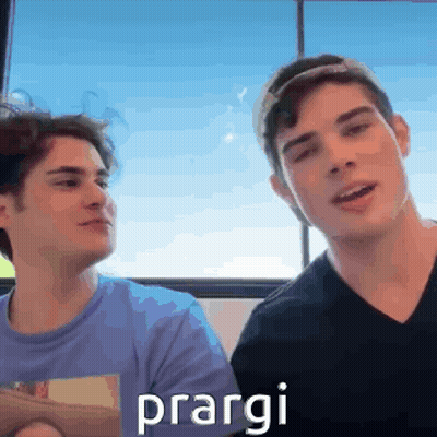 Two Young Men Are Sitting Next To Each Other In Front Of A Window And One Of Them Is Holding A Book . GIF