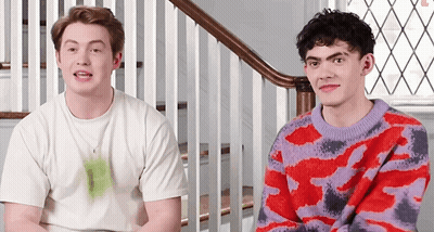 Two Young Men Are Sitting Next To Each Other On A Set Of Stairs Wearing Different Sweaters . GIF
