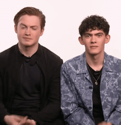 Two Young Men Are Sitting Next To Each Other With One Wearing A Floral Jacket GIF