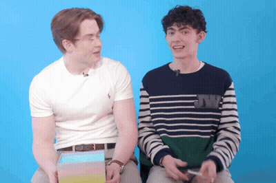 Two Young Men Are Sitting Next To Each Other With One Wearing A Sweater With Jw On It GIF