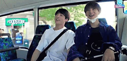 Two Young Men Are Sitting On A Bus In Front Of A Foodstore . GIF