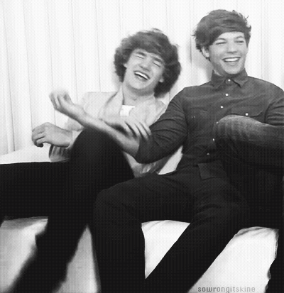 Two Young Men Are Sitting On A Couch Laughing Together . GIF