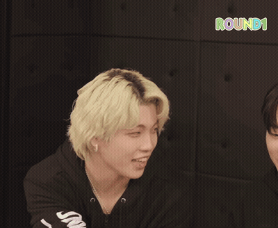 Two Young Men Are Smiling In Front Of A Sign That Says Round 1 On It GIF