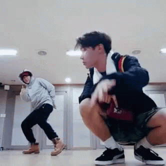 Two Young Men Are Squatting On The Floor In A Room While One Of Them Is Dancing . GIF