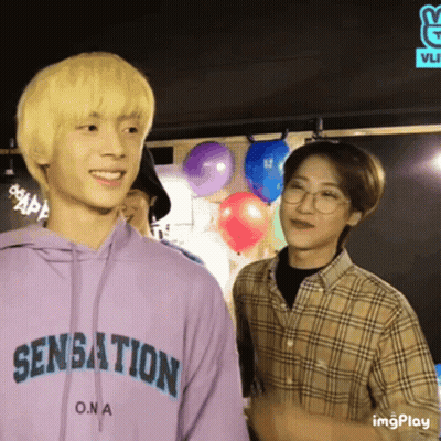 Two Young Men Are Standing Next To Each Other And One Of Them Is Wearing A Purple Hoodie That Says Sensation On It . GIF