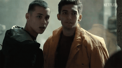 Two Young Men Are Standing Next To Each Other In A Dark Room . One Of The Men Is Wearing A Yellow Jacket . GIF