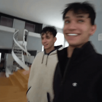 Two Young Men Are Standing Next To Each Other In A Room With A Spiral Staircase In The Background . GIF