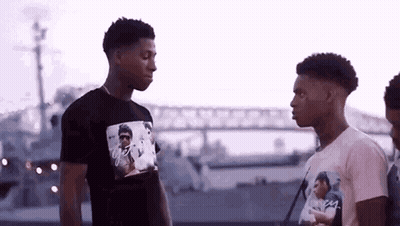 Two Young Men Are Standing Next To Each Other In Front Of A Boat . GIF