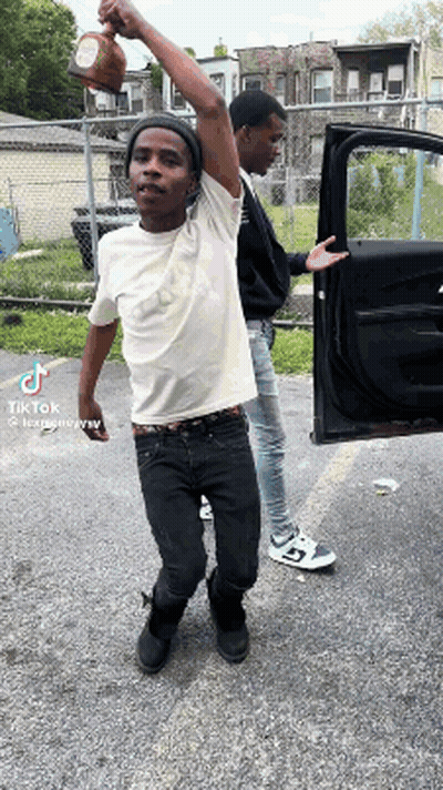 Two Young Men Are Standing Next To Each Other In Front Of A Car And One Is Holding A Bottle In His Hand . GIF