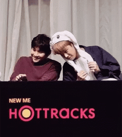 Two Young Men Are Standing Next To Each Other In Front Of A Sign That Says Hottracks GIF