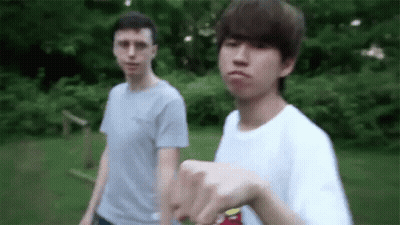 Two Young Men Are Standing Next To Each Other In The Grass . One Of The Men Is Pointing At The Camera . GIF