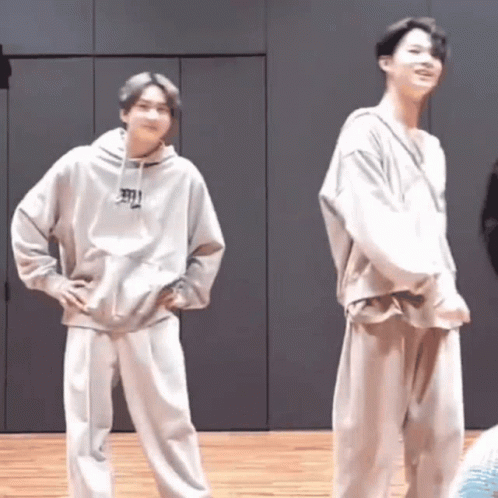 Two Young Men Are Standing Next To Each Other On A Wooden Floor In A Room . GIF