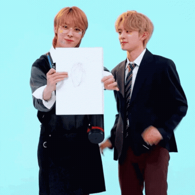 Two Young Men Are Standing Next To Each Other One Is Holding A Drawing GIF