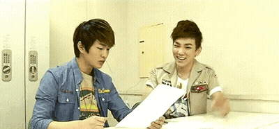 Two Young Men At Table Looking At Papers GIF