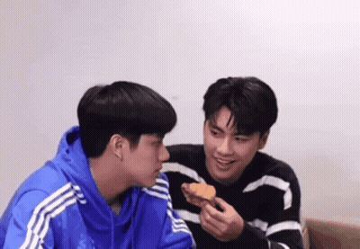 Two Young Men Eating Croissant On Couch GIF
