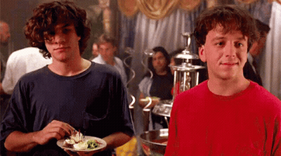 Two Young Men Holding Plates Of Food And Smiling GIF