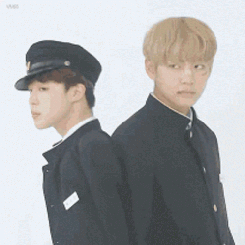 Two Young Men In Uniforms Are Standing Back To Back And One Is Wearing A Hat . GIF