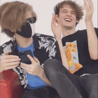 Two Young Men Laughing While Holding Cell Phone On Couch GIF