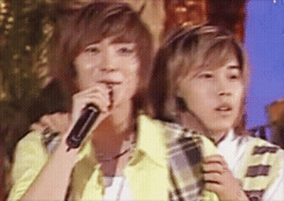 Two Young Men Singing Into Microphones While One Has A Headset On GIF
