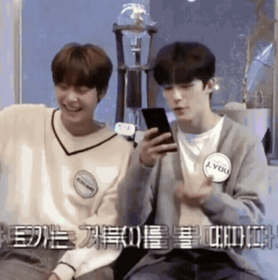 Two Young Men Sitting Next To Each Other One Looking At Phone GIF