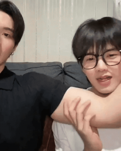 Two Young Men Sitting On Couch One Holding Other's Arm GIF
