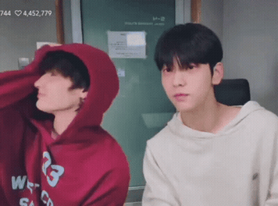 Two Young Men Sitting, One In Hoodie GIF