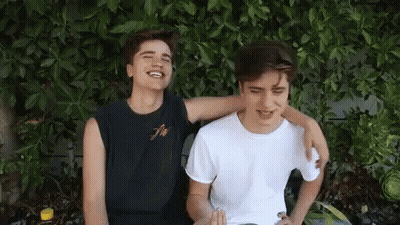 Two Young Men Sitting With Arms Around Each Other Smiling GIF