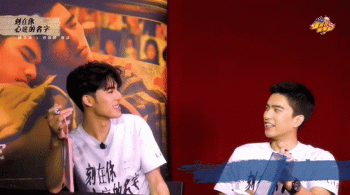 Two Young Men Talking In Front Of Chinese Poster GIF