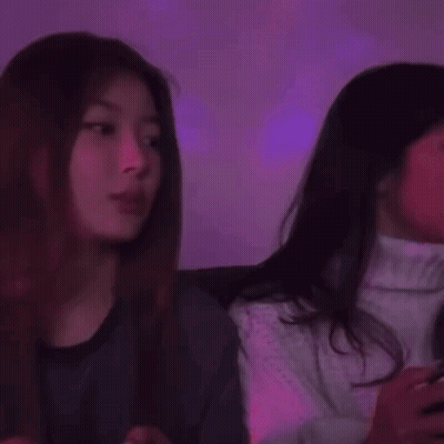 Two Young Women Are Sitting Next To Each Other In A Dark Room . GIF